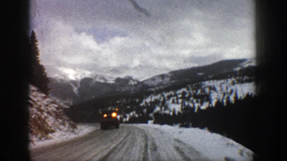 1961 Aspen winter road frame showing an approaching truck on a narrow icy track, with snowy slopes and dark trees around it.