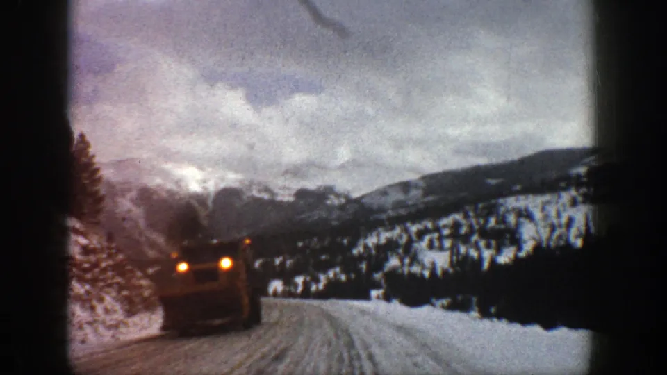 1961 Aspen 8mm frame with an oncoming truck close to the camera on an icy mountain road beneath cloudy winter peaks.