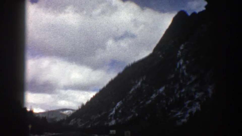 1961 Aspen road-travel frame with the camera closer to the right-hand mountain slope and cloudy sky filling the upper view.