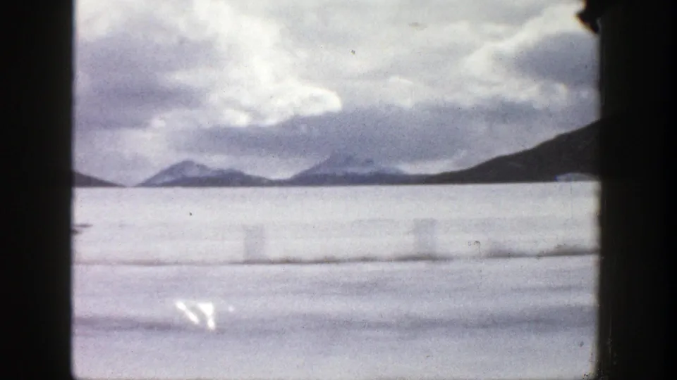 1961 Colorado 8mm frame looking through a car window toward a broad frozen lake or pale water and low mountains.