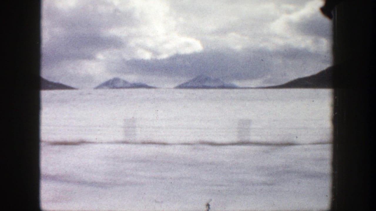 Distant snowy mountains across a pale open landscape under heavy clouds.