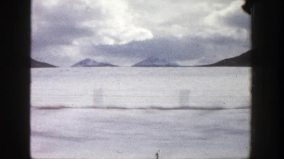 1961 Aspen-area home-movie view of distant snow-dusted mountains and a cloudy sky, seen through dark film-frame edges.