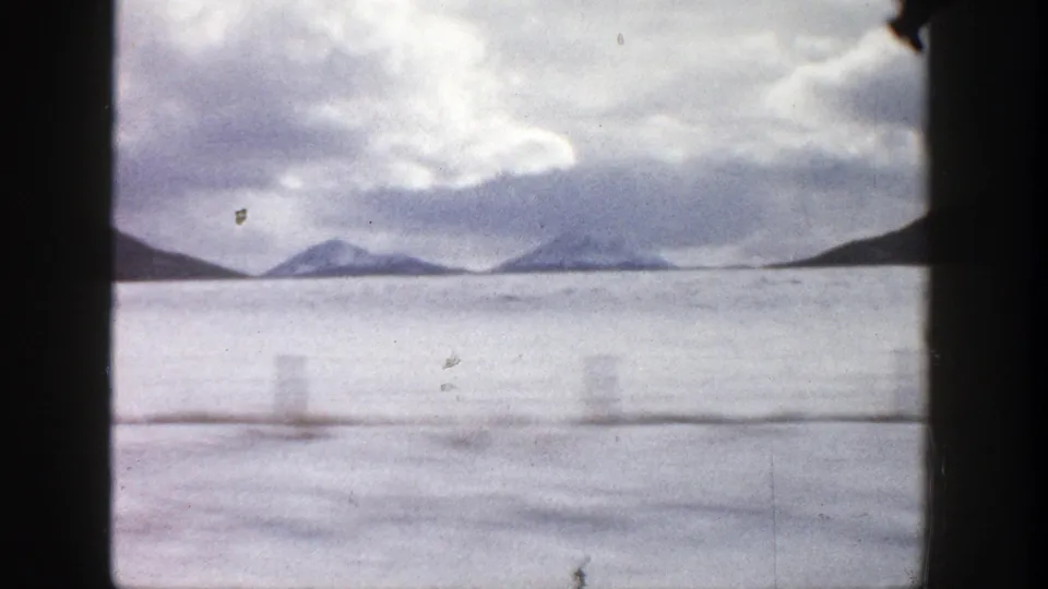 Aspen, Colorado home-movie frame with distant mountain silhouettes, pale foreground, clouded sky, and visible 8mm gate borders.
