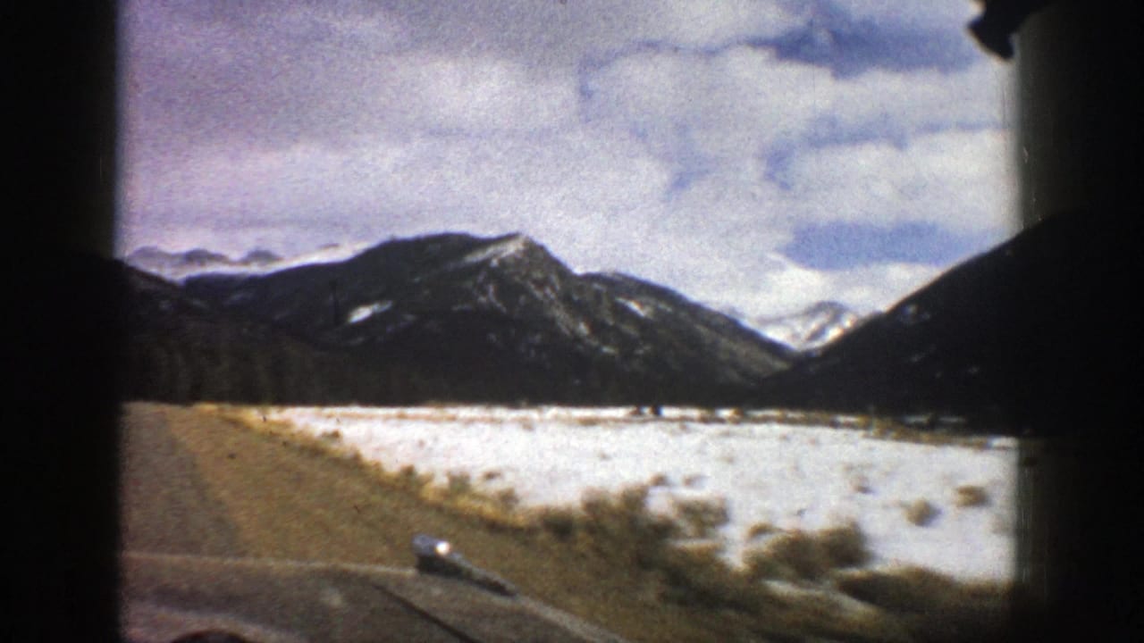 1961 Aspen-area home-movie view of a road along a snowy mountain valley, framed by dark car-window edges.