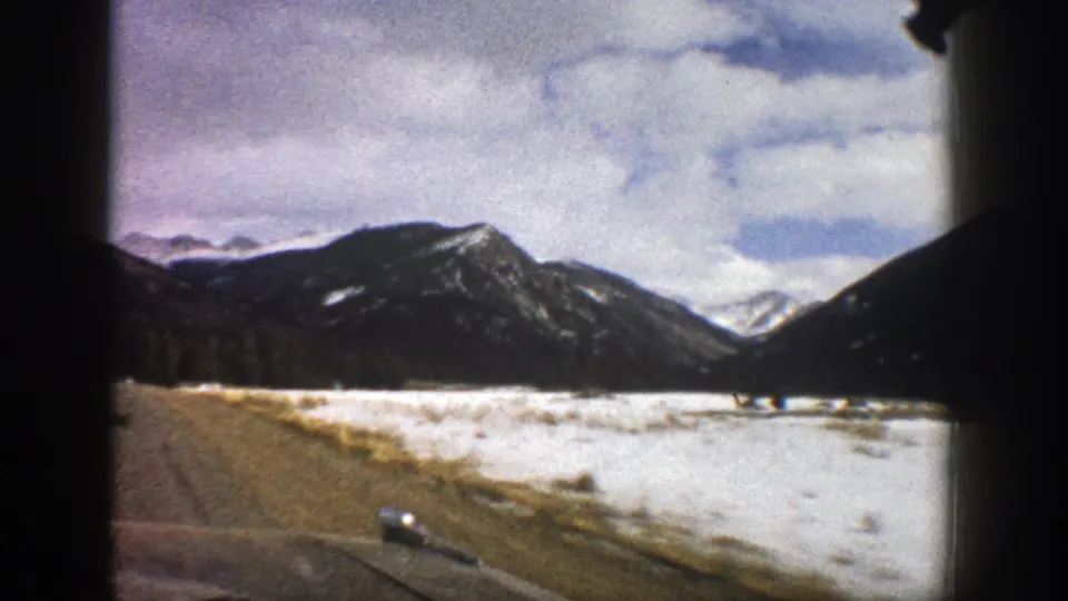 1961 Aspen, Colorado travel footage showing a roadside snowfield and dark mountain slopes through a vehicle window.