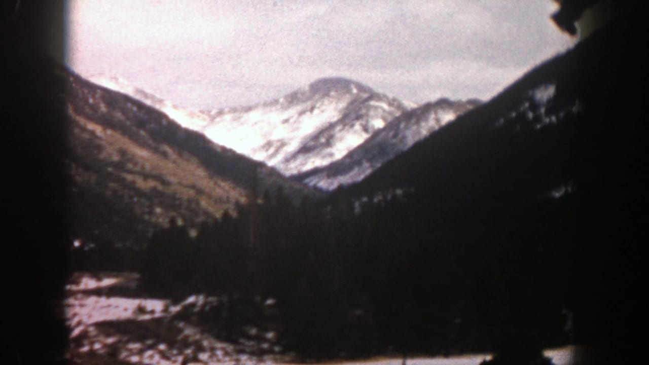 Snowy mountain peaks above a dark forested valley with soft 8mm frame edges.