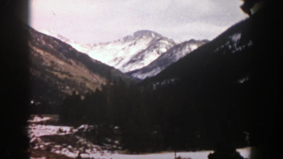 1961 Aspen, Colorado mountain landscape with bright snow on distant peaks and dark tree-covered slopes in the foreground.