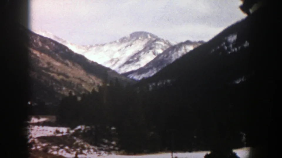 1961 Aspen, Colorado 8mm frame showing snow-bright mountains beyond a shadowed forested valley and pale winter sky.