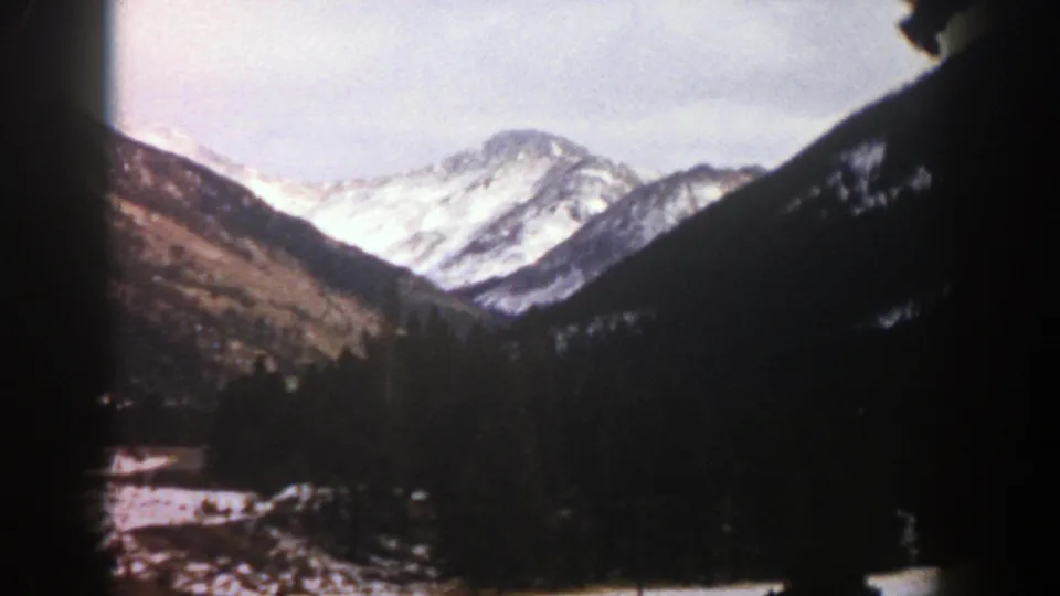 1961 Aspen, Colorado 8mm landscape with distant snowy peaks, wooded mountainsides, and darkened frame edges from the scan.