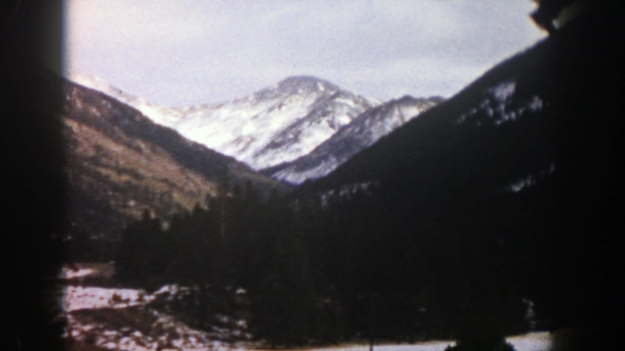 Snow-covered mountain peaks above dark forested slopes and a snowy valley edge.