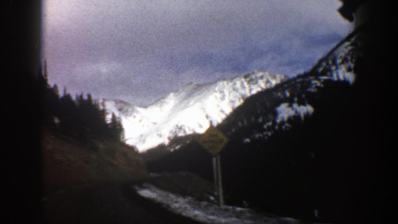 Snow-covered mountain beyond a dark winding road and roadside warning sign.