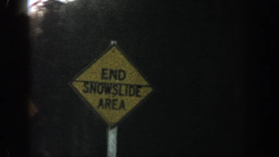 Close 8mm frame of a yellow diamond sign reading END SNOWSLIDE AREA beside the mountain road.