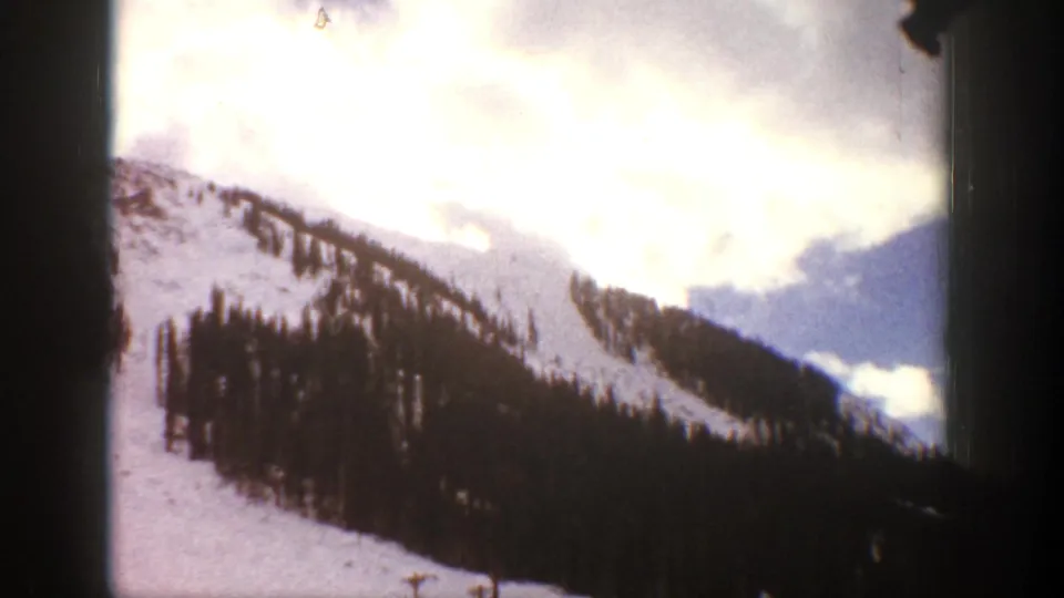 Aspen-area mountain scenery in 1961, with snow-covered slopes, evergreen trees, and bright clouded sky seen through 8mm gate edges.