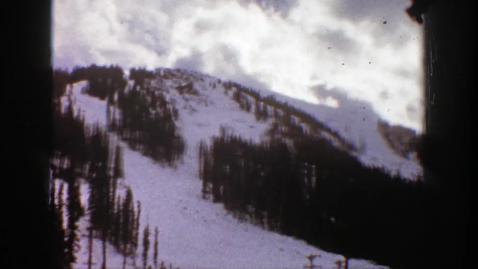 1961 Aspen, Colorado 8mm frame showing a closer snowy slope with scattered evergreen clusters, cloud cover, and black frame edges.