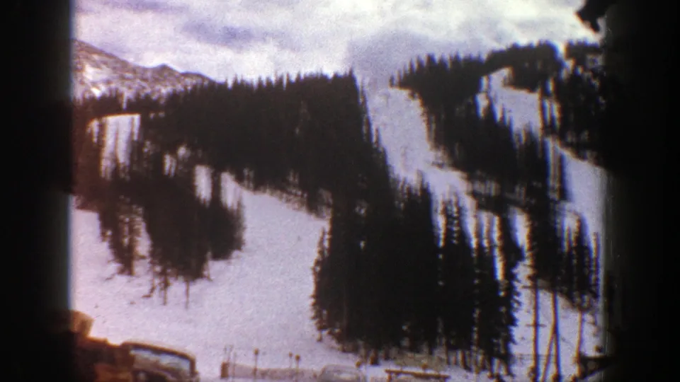 Vintage 8mm Aspen view of snow-covered slopes, evergreen stands, and a cloudy winter sky.