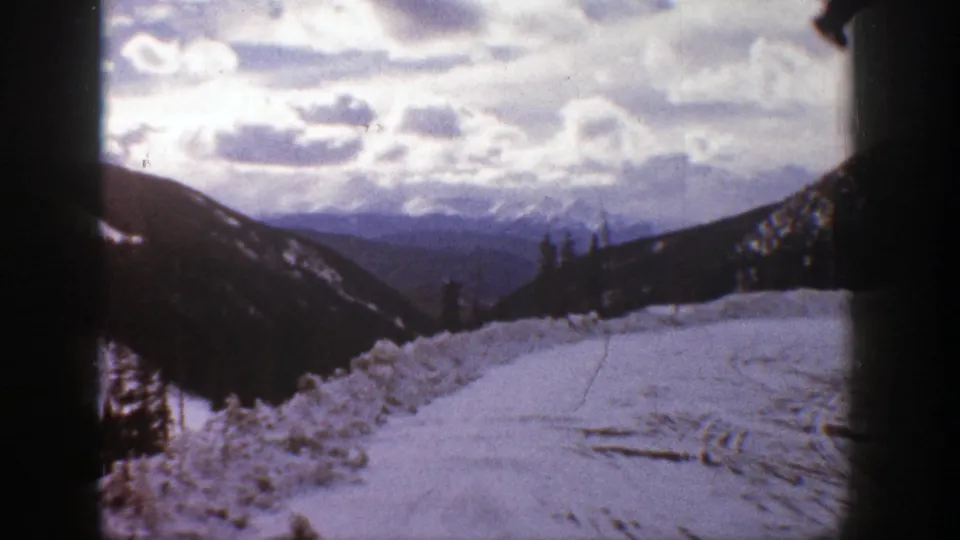 Aspen-area 1961 winter view looking along a plowed snowy road or path toward layered mountains and a cloud-filled sky.