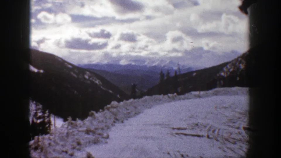 1961 Aspen-area 8mm view of a snow-covered mountain overlook, evergreen slopes, distant ridges, and a cloud-filled sky.