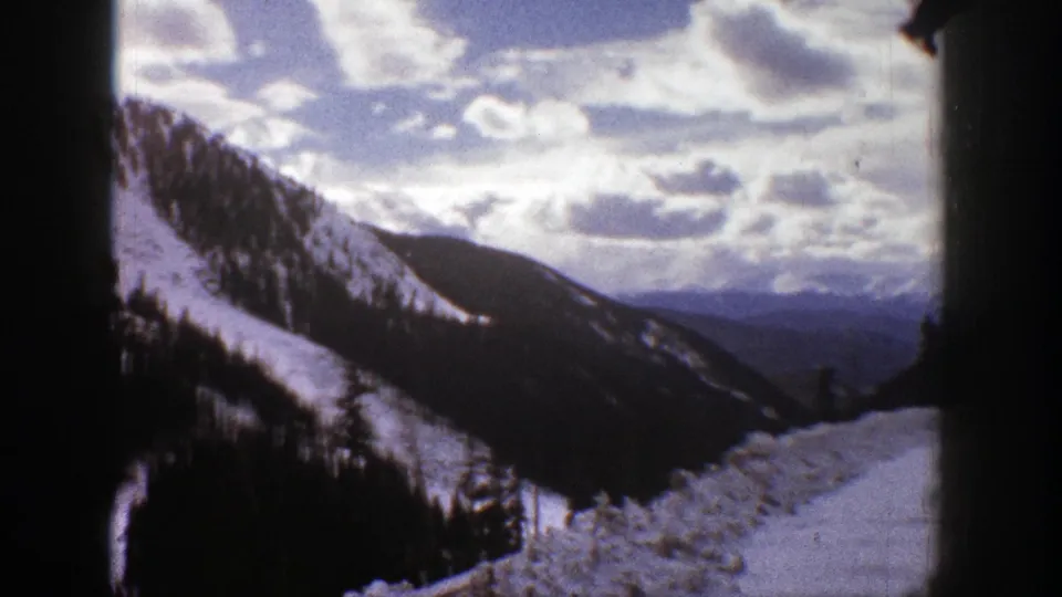Aspen-area winter landscape with a snow-covered ridge, dark evergreen forest, layered distant peaks, and visible 8mm film softness.