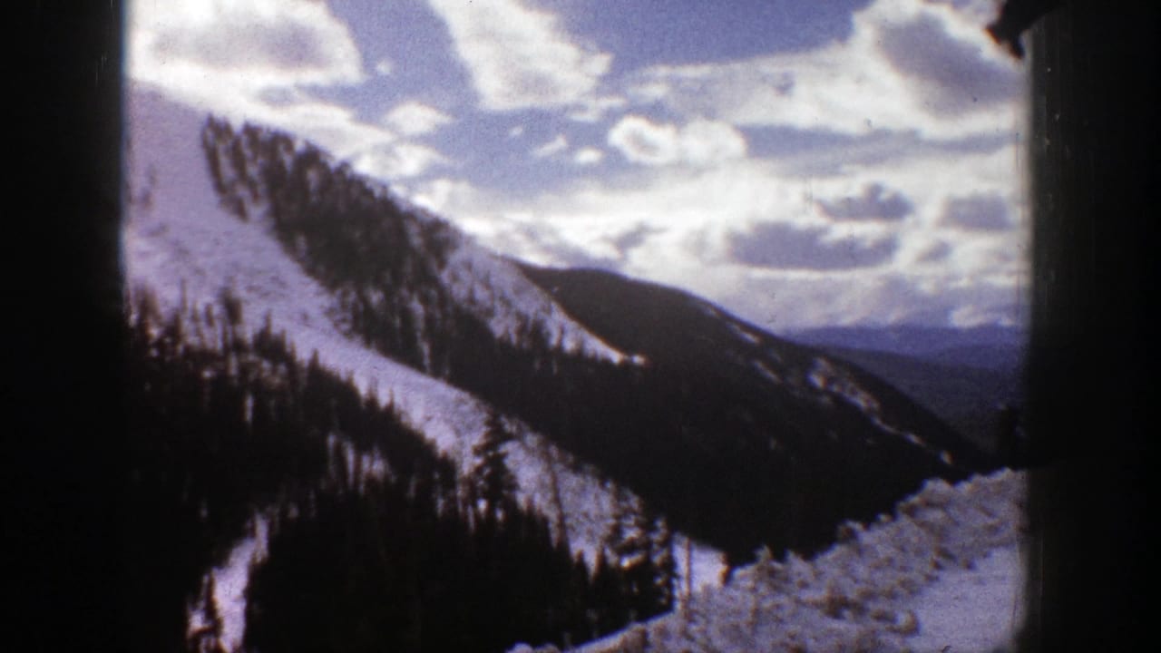 Snowy mountain slope with evergreen trees under scattered clouds.