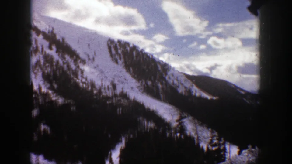 1961 Aspen mountain view with a bright snowy ridge, evergreen clusters, a shadowed valley, and scattered clouds above.