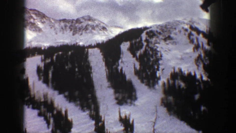 Aspen, Colorado ski terrain in 1961, with snowfields, conifer-lined runs, and dark vertical bands from the filmed frame or obstruction.