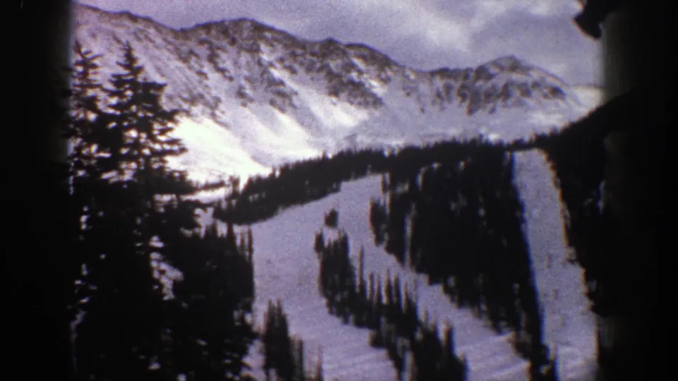 Aspen, Colorado home-movie frame from 1961 with an evergreen silhouette in front of snowy ski runs and high ridges.