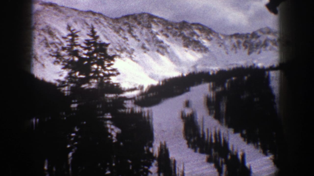 1961 Aspen, Colorado 8mm frame showing snowy peaks, dark conifers, and a winding white slope through the trees.