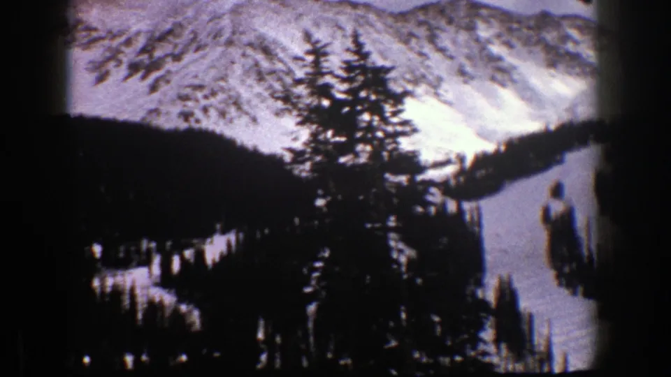 1961 Aspen, Colorado 8mm frame with conifers in the foreground and snowy alpine ridges beyond.