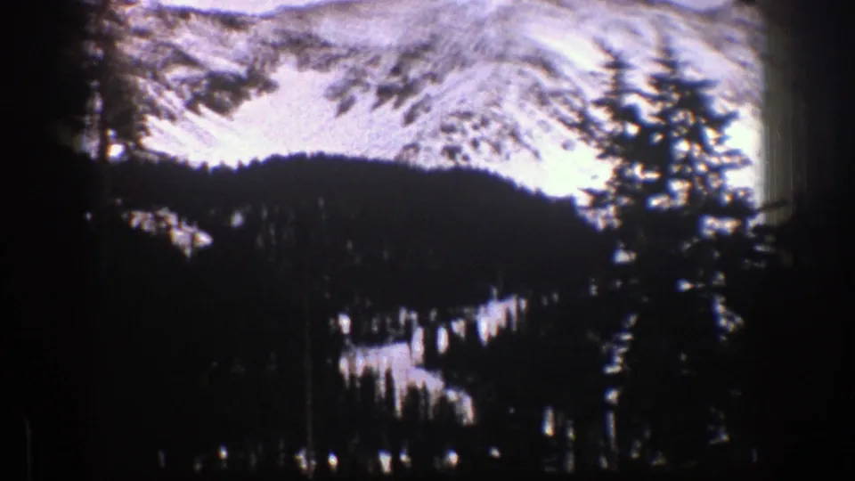 1961 Aspen, Colorado 8mm frame looking across a shaded evergreen forest toward a bright snowy ridge.
