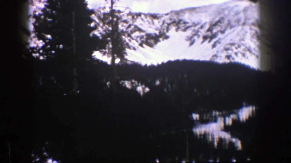 1961 Aspen, Colorado 8mm frame showing a dark conifer valley beneath bright snow-covered alpine terrain.