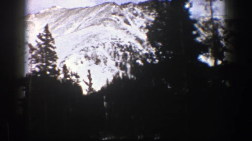 Aspen, Colorado 8mm frame with a bright snow-covered slope rising above a dark evergreen treeline and visible film border.