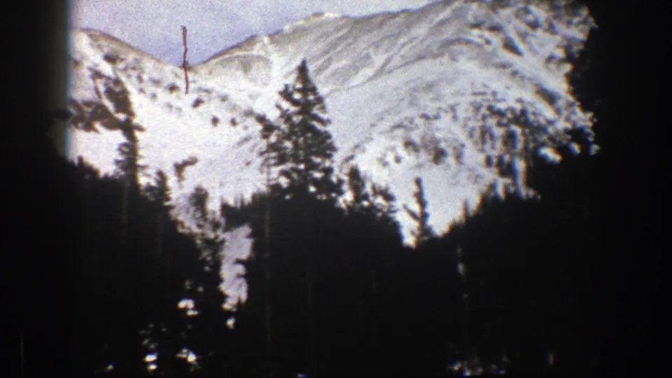 1961 Aspen landscape frame showing rugged snowy ridges and evergreen silhouettes, with home-movie grain and slight color fading.