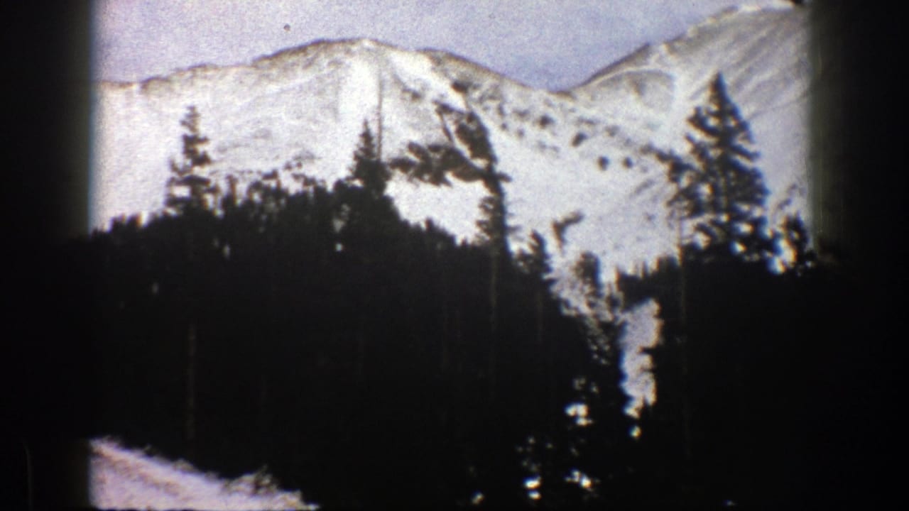 1961 Aspen, Colorado 8mm frame showing snow-covered mountains behind a dense evergreen forest.
