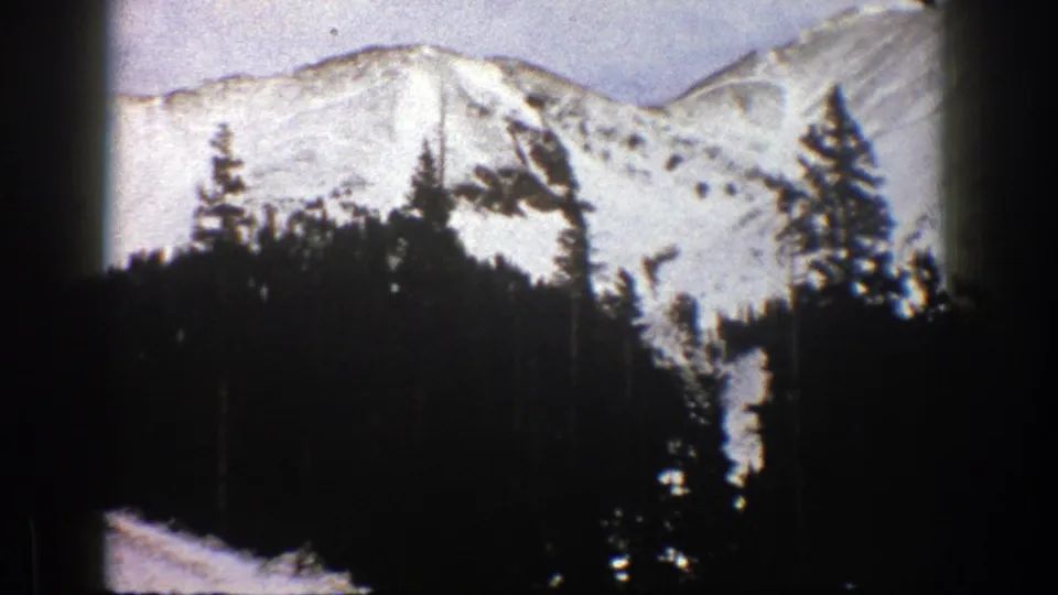 1961 Aspen, Colorado 8mm frame showing snow-covered mountains behind a dense evergreen forest.