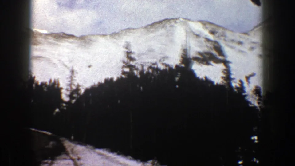 1961 Aspen, Colorado home-movie frame with snowy ridges, evergreens, and a partial road area below.