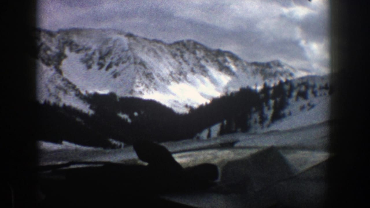 Snow-covered mountain ridge seen through a dark vehicle window frame.