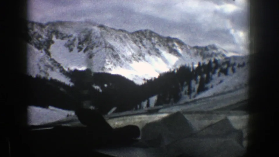 Aspen, Colorado winter landscape from a 1961 8mm home movie, showing snowfields, a forested ridge, and vehicle-window framing.
