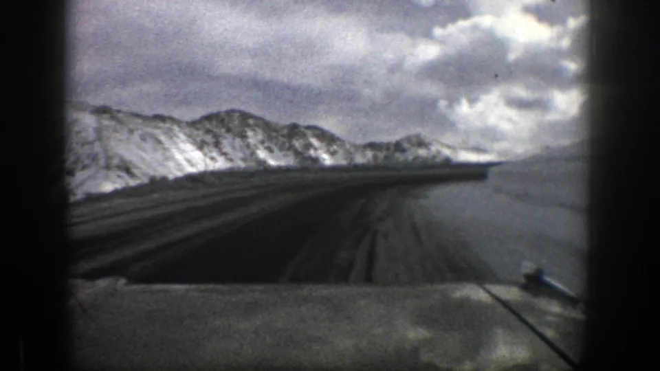 In-car 8mm view near Aspen, Colorado, showing a snowy roadway curving along mountain terrain in 1961.