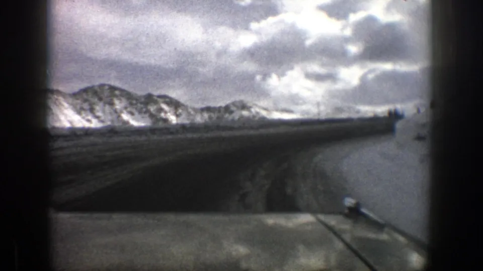 End frame of the 1961 Aspen-area drive, looking through the windshield across the hood toward snowbanks and mountains.