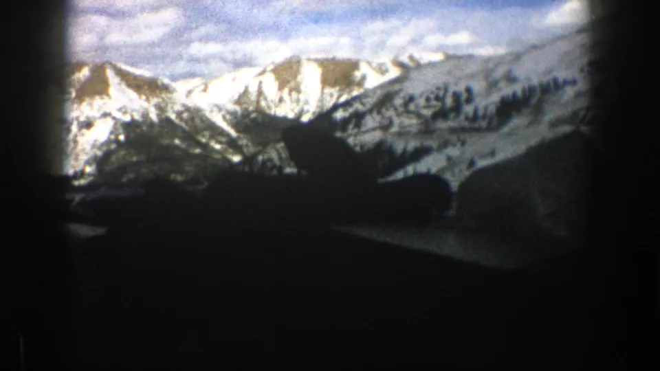 Snowy Colorado mountain peaks fill the windshield view, partly framed by dark car interior shapes and roadside winter terrain.