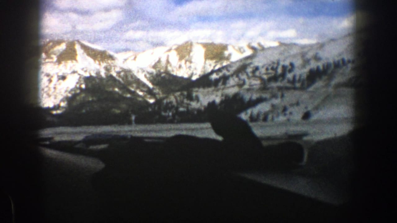 Snowy mountain view through a car windshield with dashboard silhouette in foreground.