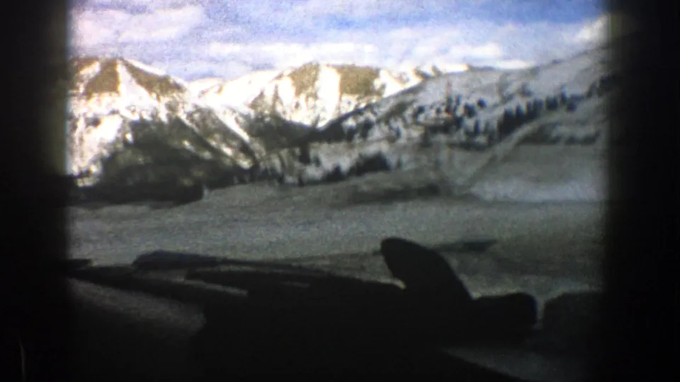 The vehicle view opens toward a snow-covered Aspen, Colorado mountain slope with dark windshield edges and dashboard below.