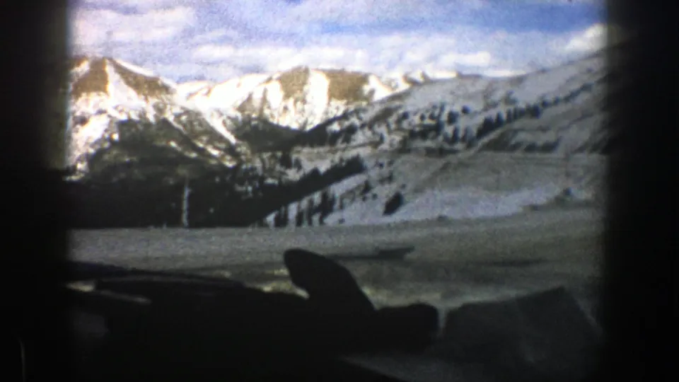 A late-frame windshield view shows snowy Aspen-area slopes, evergreen lines, and bright mountain peaks beyond the dashboard.