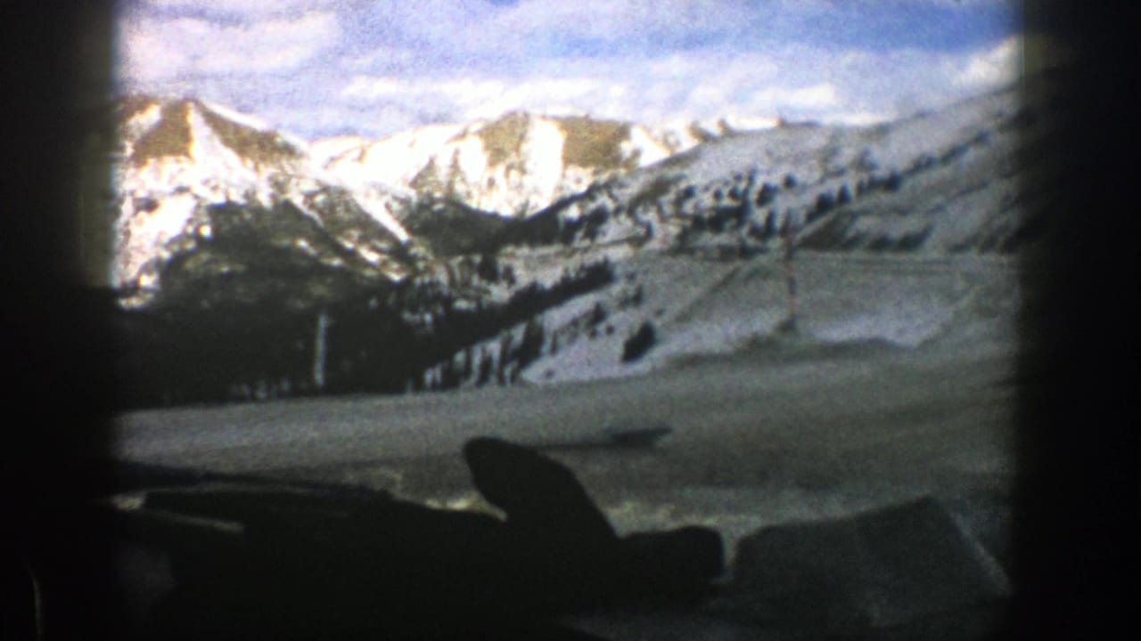 1961 Aspen, Colorado home-movie frame showing snow-covered peaks and a road viewed from inside a moving car.