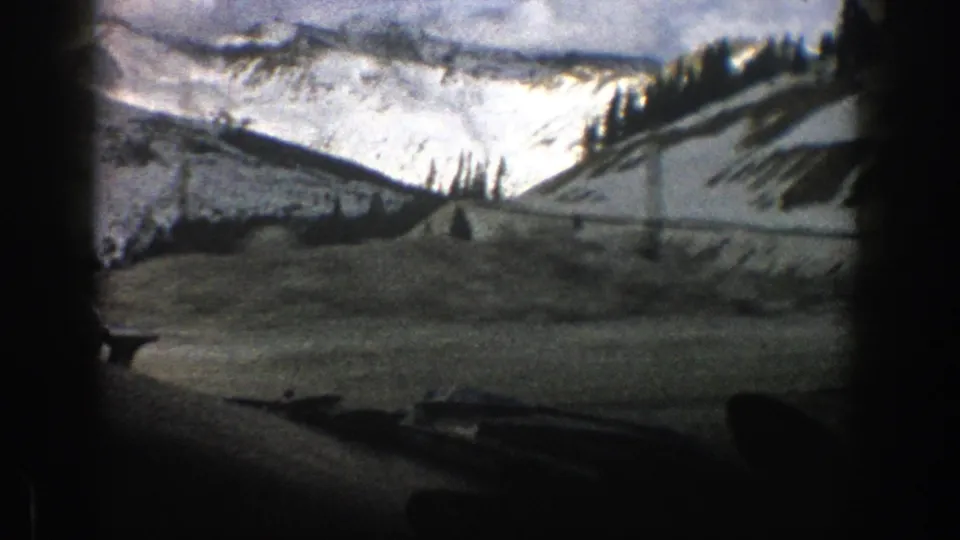 Soft 8mm frame of a snowy Aspen mountain route with roadside snow, scattered evergreens, and steep white slopes.