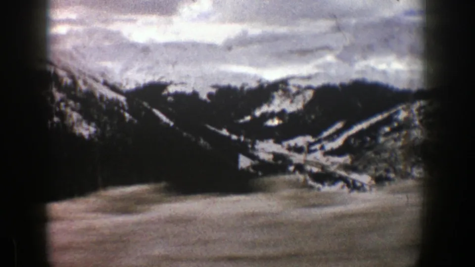 Aspen, Colorado winter landscape with dark trees, pale snowfields, and distant mountains, framed by 8mm home-movie edge shadows.