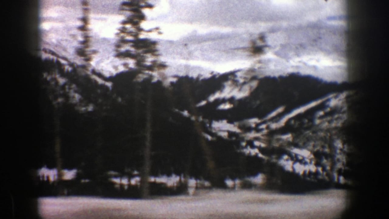 Snowy mountain valley with evergreen trees and dark film borders.