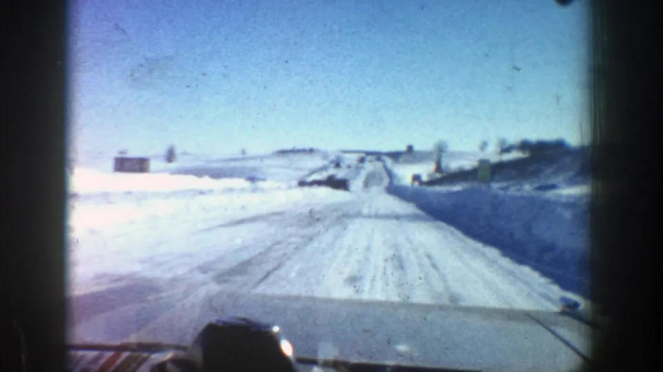 Forward view from a moving car on a snow-lined road near Aspen, Colorado, with tire tracks and open winter terrain.