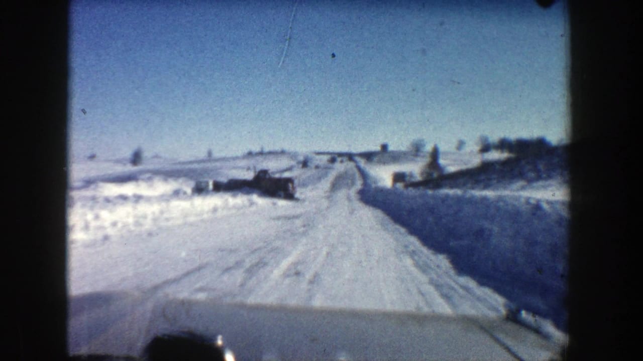 Snow-covered road seen from inside a vehicle, with a parked truck on the left.