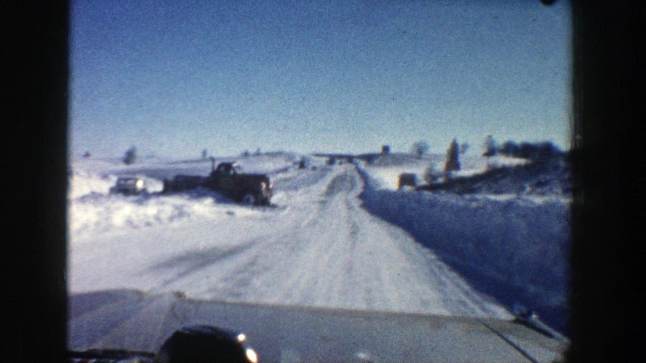Snowy road curves ahead with truck and snowbanks visible along the left side.